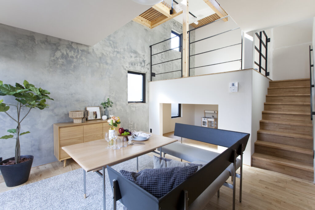 モルタル調のアクセントウォールと吹き抜けが特徴的な、開放感のあるリビングダイニング