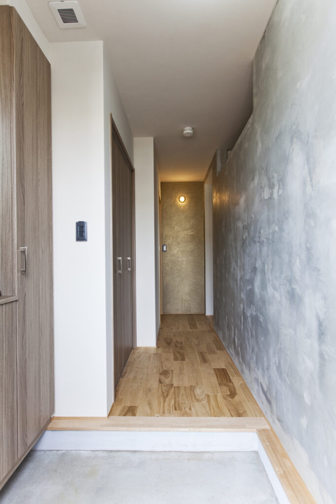 木目調の建具とグレーの塗り壁が続く、シンプルで洗練された玄関ホールの内廊下