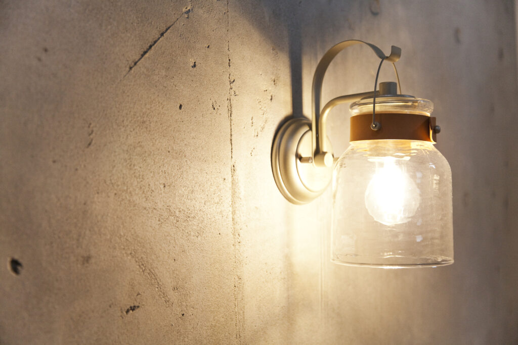 コンクリート打ちっぱなし風の壁に取り付けられた、温かな光を放つガラス瓶型のアンティーク調ブラケットライト