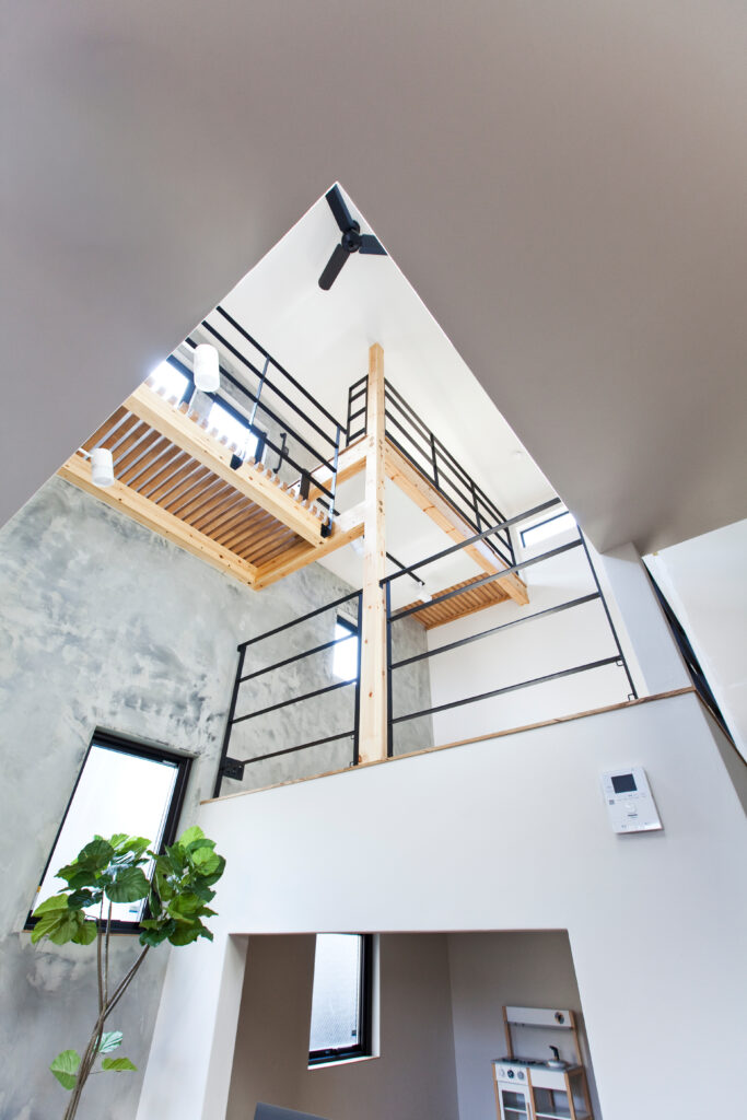 木造の梁と黒いスチール手すりがスタイリッシュな吹き抜け空間を見上げた構図