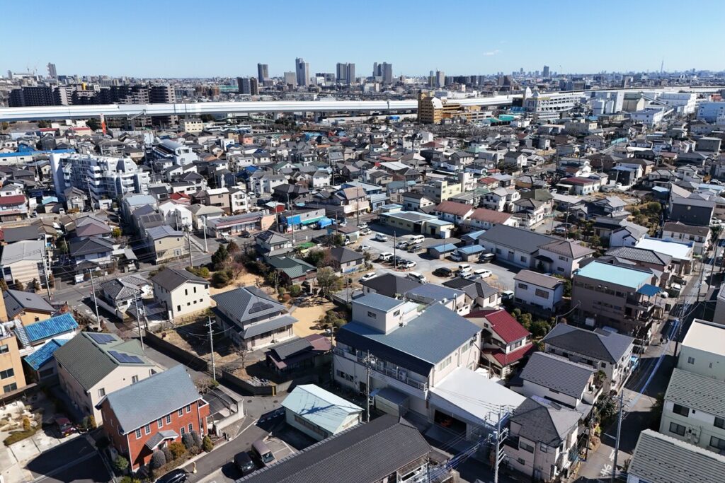 多くの住宅が立ち並び、遠くにビル群が見える晴天の街並みを捉えた俯瞰写真