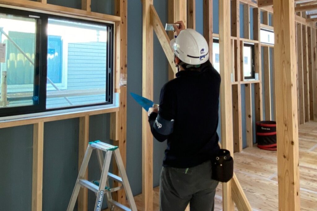 建築中の現場で、スマートフォンのカメラを使用して柱や接合部の施工状況を記録するスタッフ