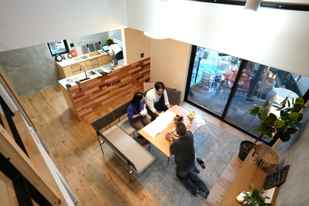 吹き抜け上部から見下ろした、ダイニングテーブルを囲んで打ち合わせをする夫婦とスタッフ