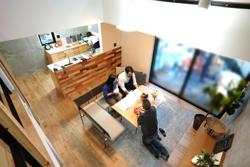吹き抜け上部から見下ろした、ダイニングテーブルを囲んで打ち合わせをする夫婦とスタッフ