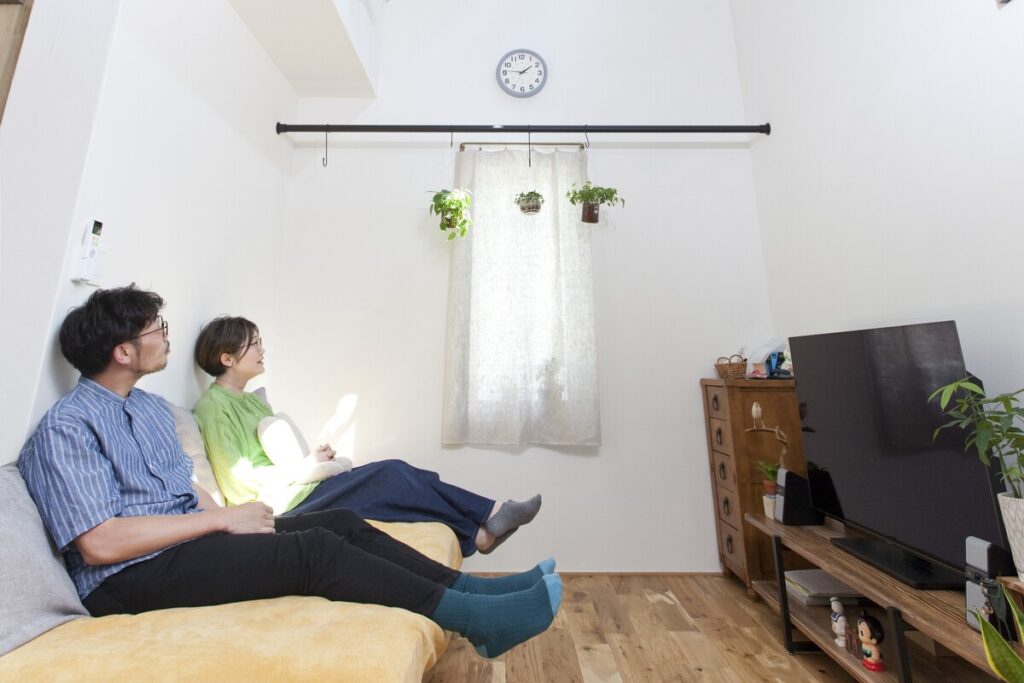 吹き抜けのあるリビングのソファで、ゆったりとくつろぎながらテレビを眺めるご夫婦の日常風景