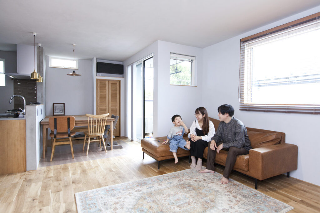 窓から日差しが入った明るく暖かな雰囲気のリビングソファで、家族が談笑している様子