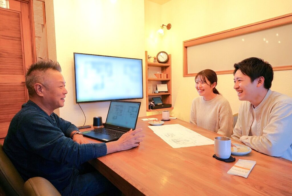 注文住宅の打ち合わせで、設計図や資料を広げて専門スタッフと笑顔で話し合うご夫婦の様子