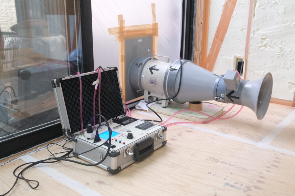 建築現場の窓に設置された気密測定器と、断熱等級6の性能を裏付けるC値測定の様子